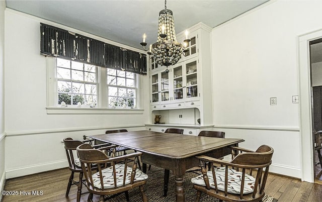 dining space with dark wood-type flooring, a notable chandelier, and ornamental molding