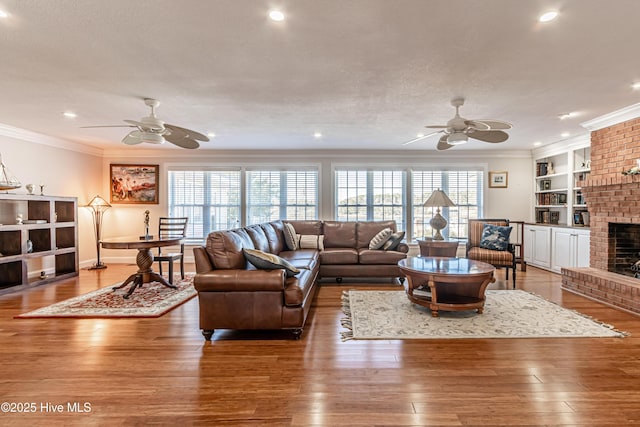 living room featuring built in features, wood-type flooring, a brick fireplace, and ceiling fan