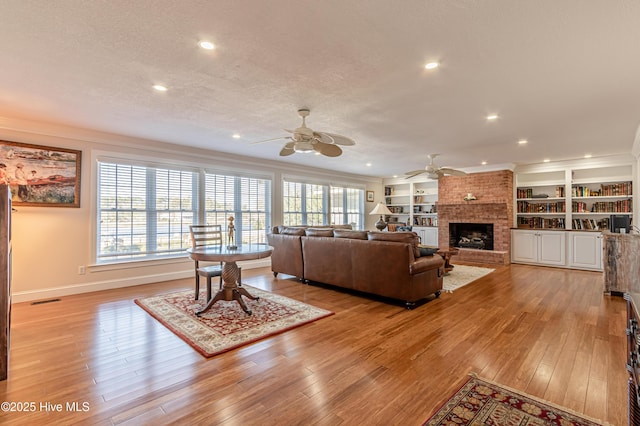 living room with a fireplace, light wood-type flooring, a textured ceiling, and crown molding