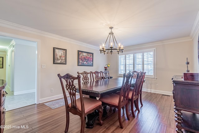 dining area with hardwood / wood-style floors, ornamental molding, and an inviting chandelier