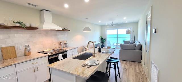 kitchen with tasteful backsplash, a breakfast bar, custom range hood, sink, and white cabinetry