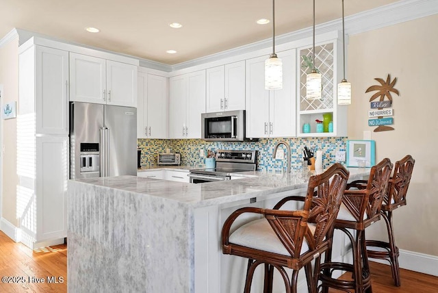 kitchen with light stone countertops, white cabinets, pendant lighting, and appliances with stainless steel finishes