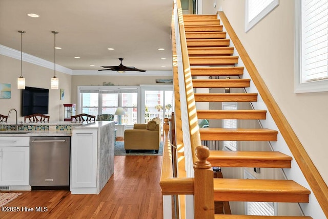 staircase featuring wood-type flooring, ceiling fan, ornamental molding, and sink