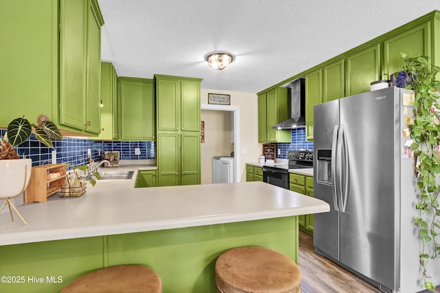 kitchen with kitchen peninsula, washer and clothes dryer, wall chimney exhaust hood, and stainless steel appliances