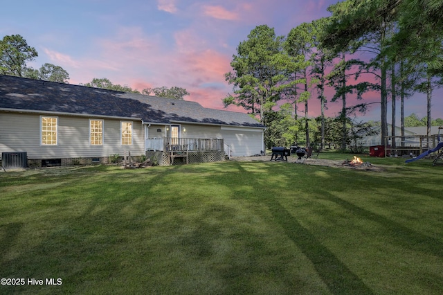 back house at dusk with a lawn, a fire pit, a deck, and central AC