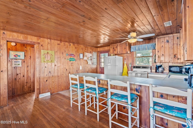 kitchen with kitchen peninsula, white appliances, wood ceiling, and wood walls