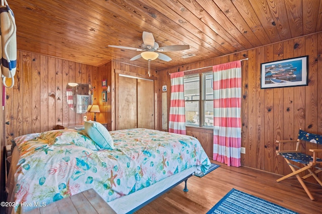 bedroom with wood walls, a closet, ceiling fan, and hardwood / wood-style floors