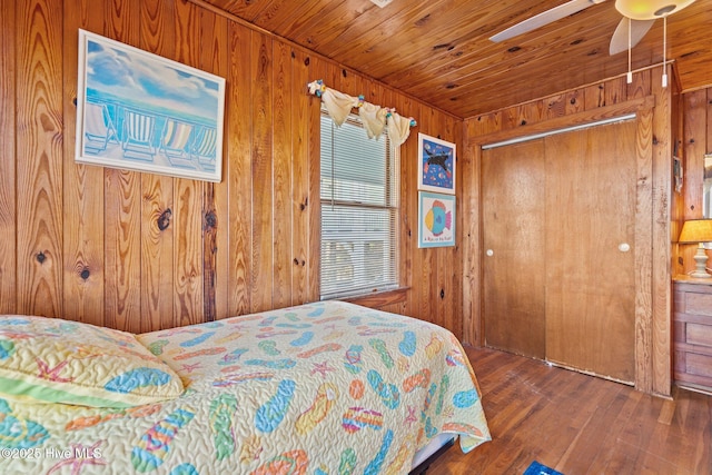 bedroom with a closet, hardwood / wood-style flooring, ceiling fan, and wooden walls