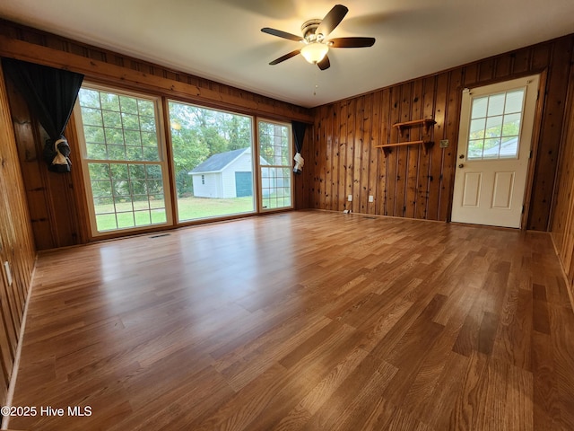 unfurnished living room with ceiling fan, wooden walls, and wood-type flooring