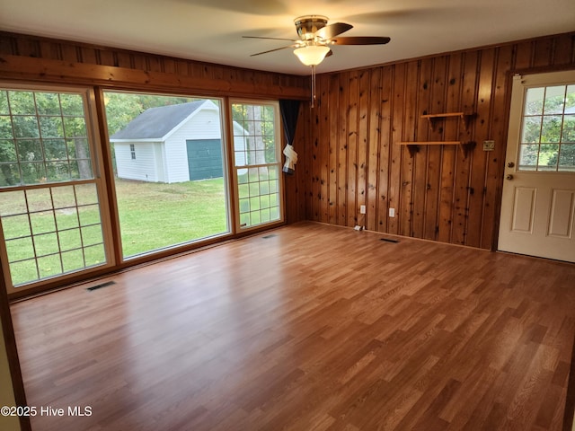 unfurnished living room featuring ceiling fan, hardwood / wood-style floors, and wooden walls