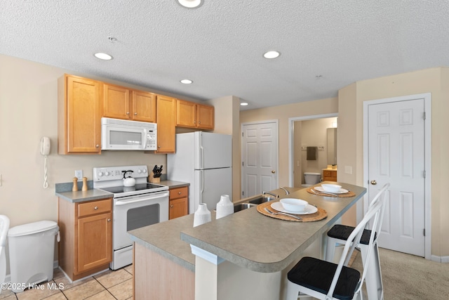 kitchen featuring a kitchen bar, sink, white appliances, and a textured ceiling