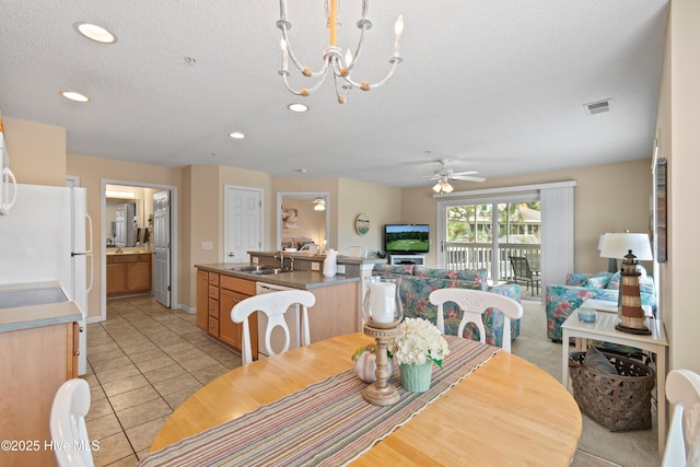 tiled dining room featuring ceiling fan with notable chandelier, sink, and a textured ceiling