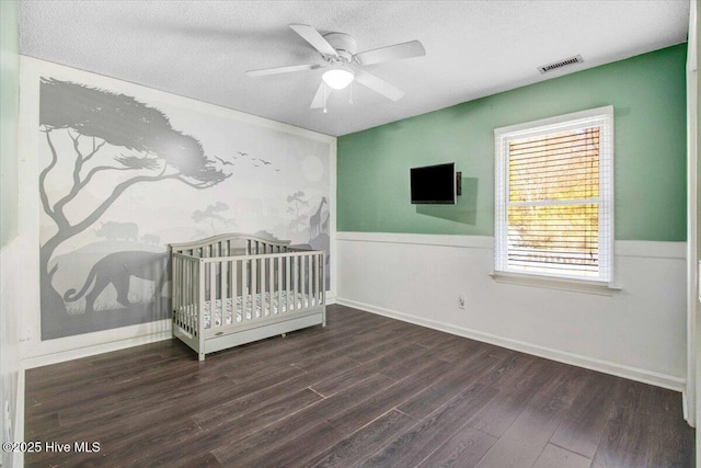 unfurnished bedroom with a textured ceiling, ceiling fan, dark wood-type flooring, and a nursery area