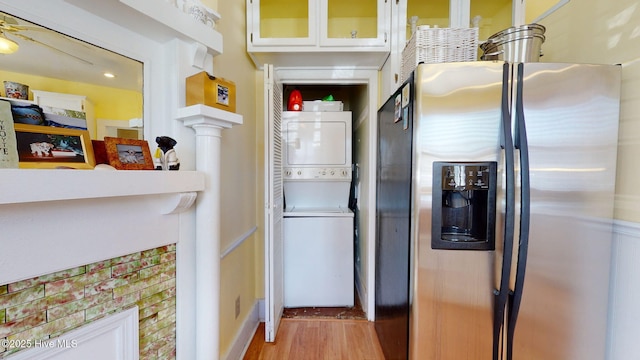 kitchen with white cabinetry, ceiling fan, stacked washing maching and dryer, stainless steel fridge, and light wood-type flooring