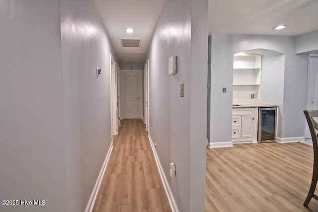 hallway with light wood-type flooring, built in features, and beverage cooler