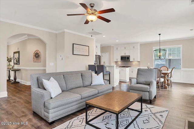 living room featuring ceiling fan with notable chandelier, dark wood-type flooring, and ornamental molding