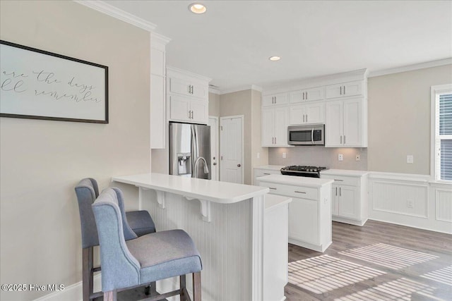 kitchen with white cabinetry, a breakfast bar area, appliances with stainless steel finishes, dark hardwood / wood-style floors, and ornamental molding