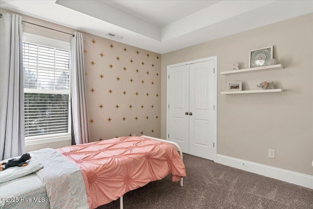 carpeted bedroom with a closet and a raised ceiling