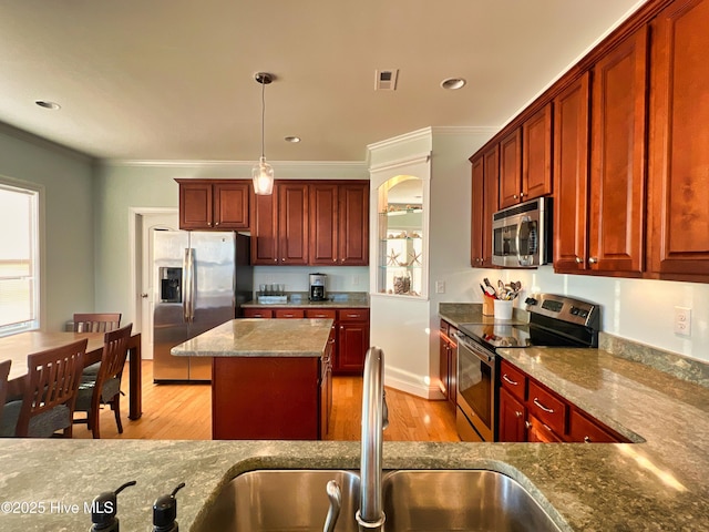 kitchen featuring stainless steel appliances, sink, decorative light fixtures, light hardwood / wood-style flooring, and a kitchen island