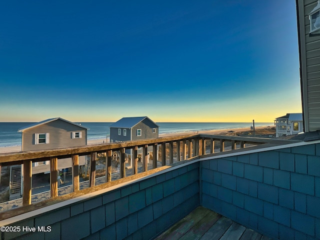 balcony at dusk featuring a view of the beach and a water view