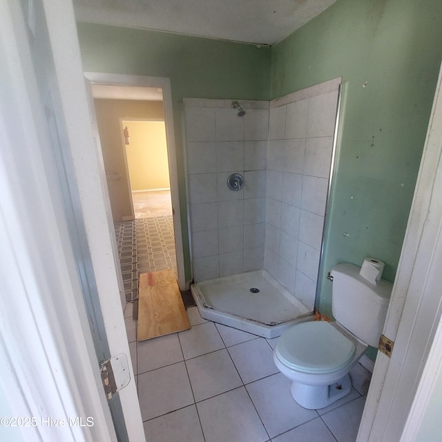 bathroom with toilet, tile patterned flooring, and tiled shower