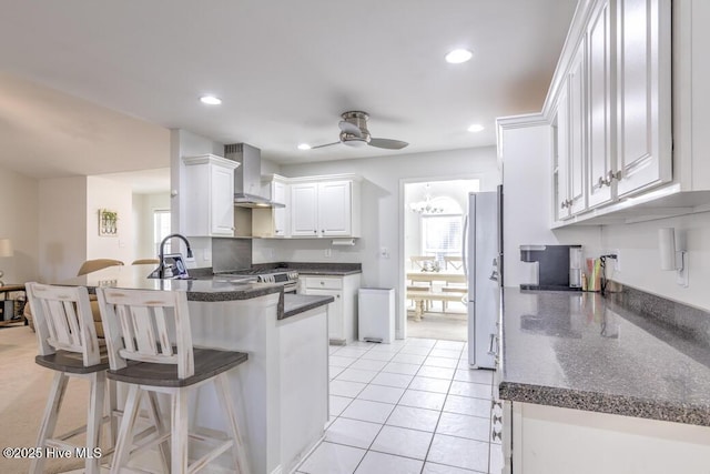 kitchen with white cabinets, a kitchen breakfast bar, wall chimney exhaust hood, kitchen peninsula, and stainless steel appliances