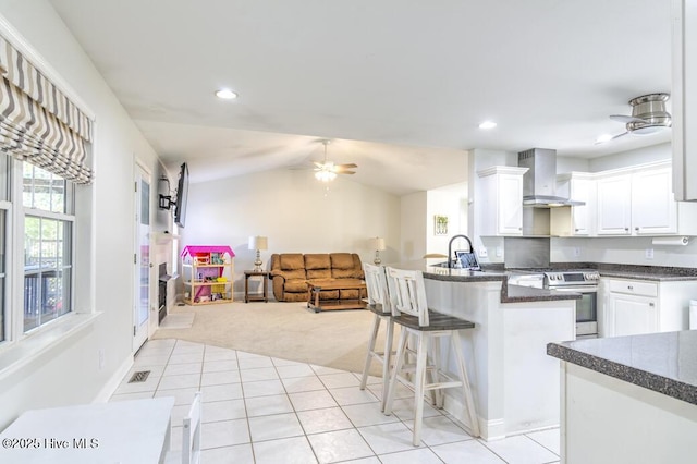 kitchen featuring wall chimney range hood, a kitchen breakfast bar, light colored carpet, stainless steel electric range, and white cabinets