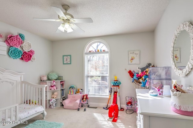 bedroom featuring a textured ceiling, ceiling fan, a crib, and carpet floors