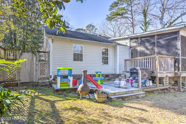 rear view of property featuring a deck, a lawn, and a sunroom