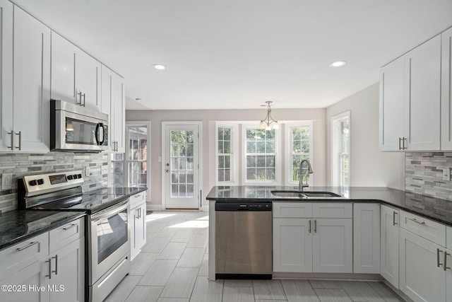 kitchen with white cabinetry, kitchen peninsula, stainless steel appliances, backsplash, and sink