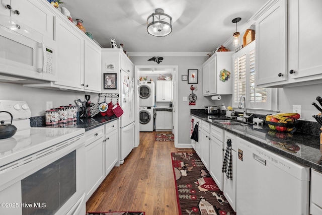 kitchen featuring white appliances, white cabinets, sink, hanging light fixtures, and stacked washing maching and dryer