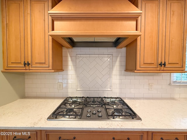 kitchen featuring decorative backsplash, custom exhaust hood, light stone countertops, and stainless steel gas cooktop