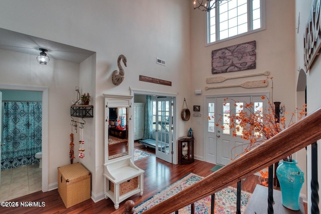 entryway with hardwood / wood-style floors, a towering ceiling, and a notable chandelier