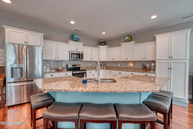 kitchen with a kitchen island with sink, white cabinetry, sink, and appliances with stainless steel finishes