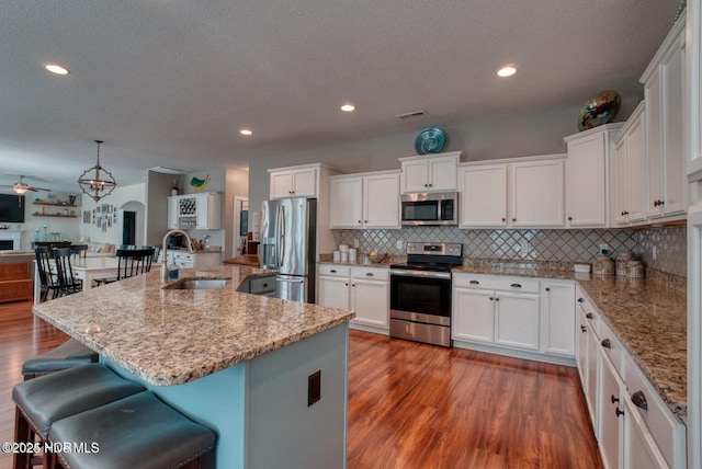 kitchen featuring appliances with stainless steel finishes, sink, decorative light fixtures, white cabinetry, and an island with sink