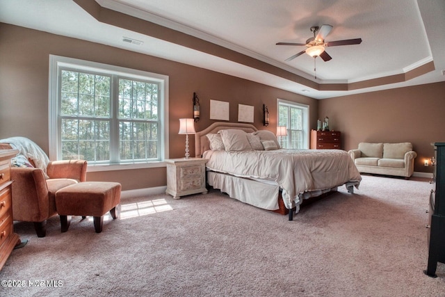 carpeted bedroom featuring ceiling fan, ornamental molding, multiple windows, and a tray ceiling