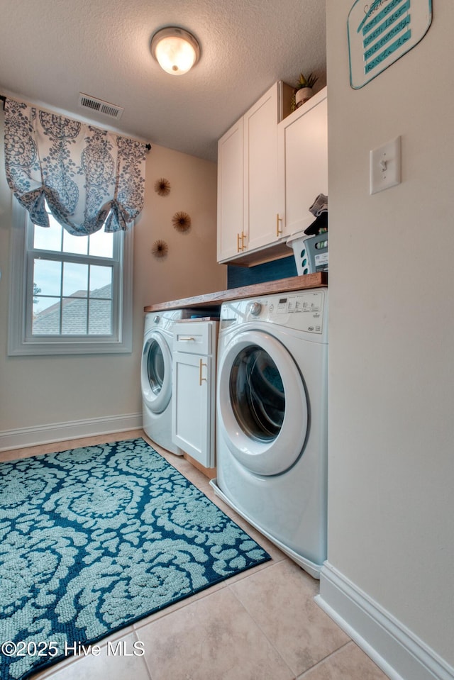 clothes washing area featuring washer and dryer, light tile patterned flooring, cabinets, and a textured ceiling