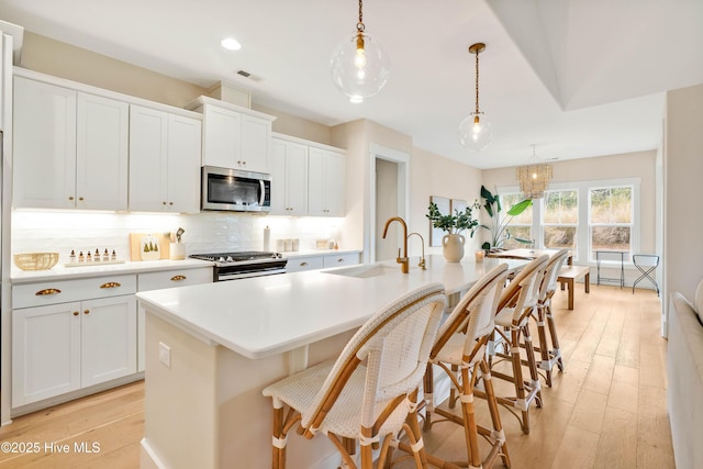 kitchen featuring stainless steel appliances, a kitchen island with sink, hanging light fixtures, and white cabinetry