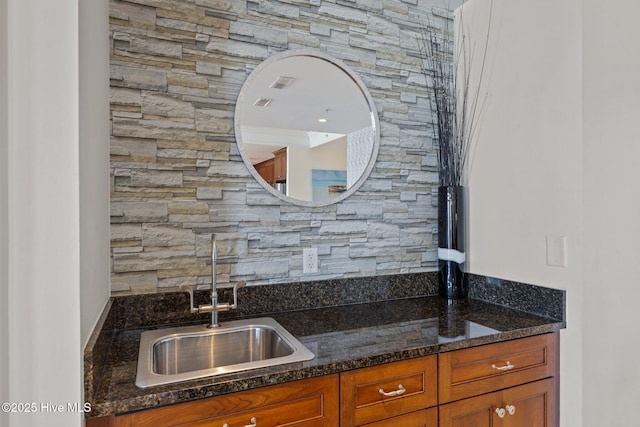 kitchen featuring brown cabinetry, dark stone counters, and a sink