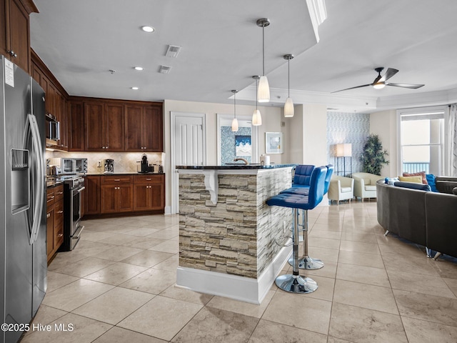 kitchen featuring pendant lighting, a center island, a kitchen breakfast bar, ceiling fan, and appliances with stainless steel finishes