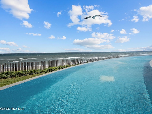 view of pool featuring fence, a view of the beach, and a water view