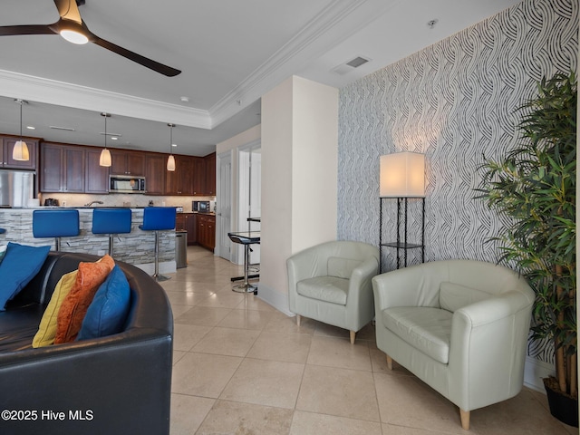 living area featuring baseboards, an accent wall, ceiling fan, crown molding, and light tile patterned floors