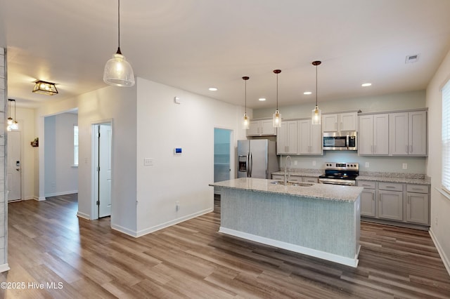 kitchen with stainless steel appliances, a kitchen island with sink, sink, pendant lighting, and hardwood / wood-style flooring