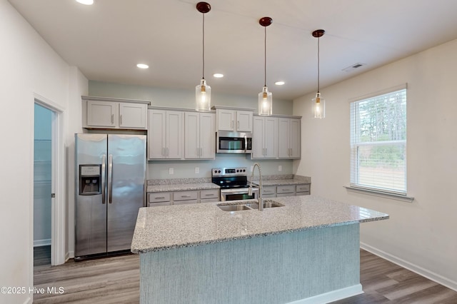 kitchen featuring light stone countertops, sink, light hardwood / wood-style floors, pendant lighting, and appliances with stainless steel finishes