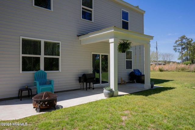 back of property with a fire pit, a patio area, and a lawn