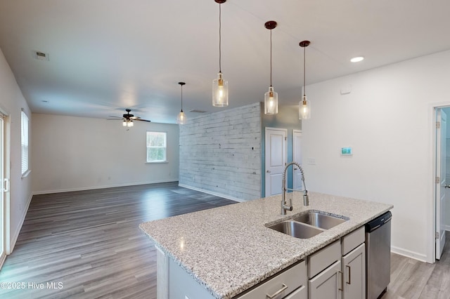 kitchen with light stone countertops, ceiling fan, sink, a center island with sink, and dishwasher