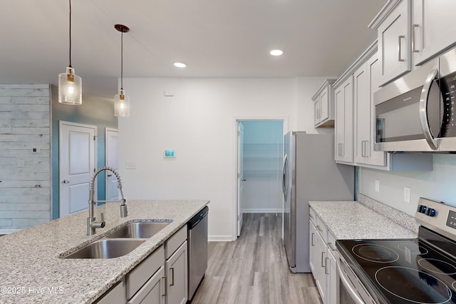 kitchen with light stone countertops, appliances with stainless steel finishes, light wood-type flooring, sink, and decorative light fixtures