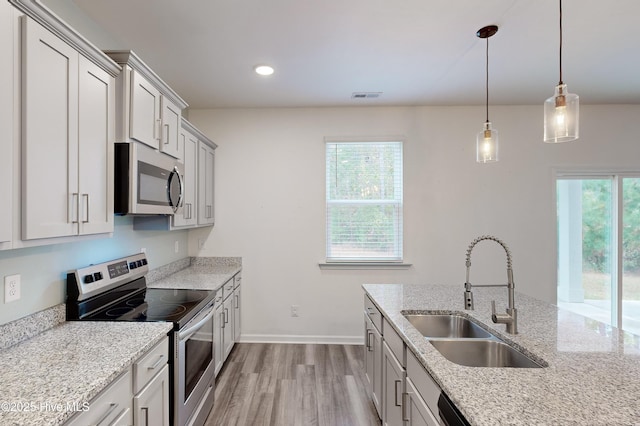 kitchen featuring sink, light wood-type flooring, appliances with stainless steel finishes, decorative light fixtures, and light stone counters