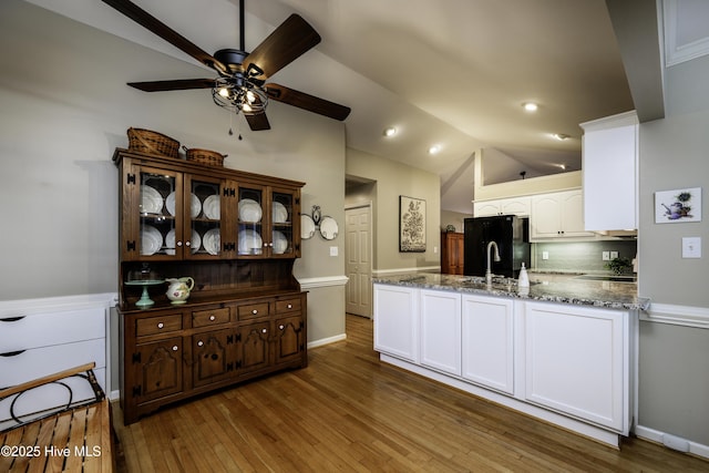 kitchen featuring black refrigerator, vaulted ceiling, decorative backsplash, dark stone countertops, and white cabinetry