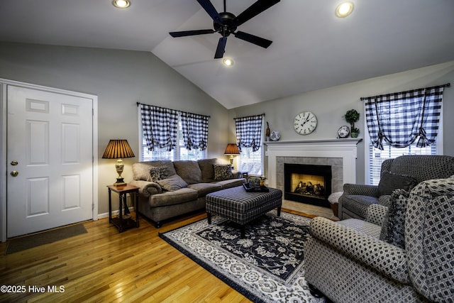 living room with a tile fireplace, wood-type flooring, vaulted ceiling, and a healthy amount of sunlight